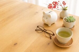 木のテーブルに置いた豚の貯金箱と眼鏡と緑茶